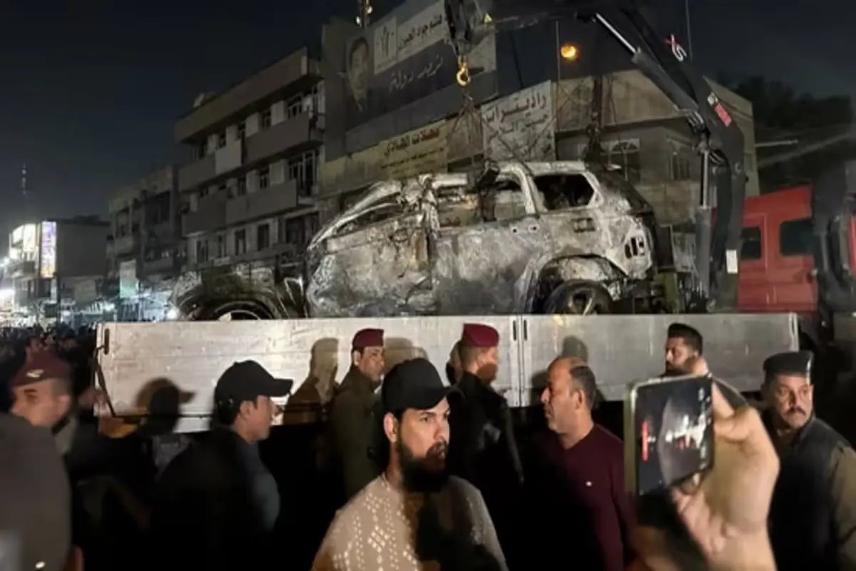 Crowds gather around damaged vehicle in Baghdad after alleged drone strike.